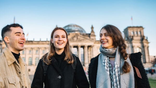 En grupp om tre personer pratar glatt framför Riksdagshuset i Berlin - efter kurs i tyska
