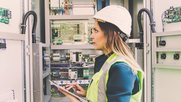 Service engineer wearing white helmet standing, working, checking conducts front of a control panel read and writing notes with digital tablet in energy control room of modern power plant electric energy station. 