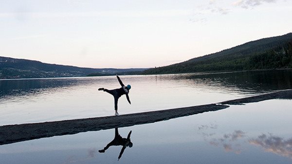 Kvinna i danspose på landremsa vid sjö