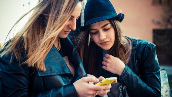 Två studiekamrater tittar i sina mobilerpå information från Folkuniversitetet Komvux Södertälje