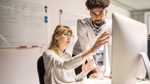 Multi-ethnic businesswoman and businessman discussing over computer at desk in creative office