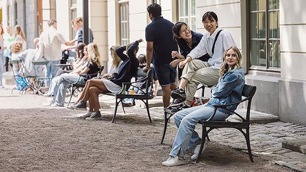 Tre elever på Kungstensgymnasiet sitter på en parkbänk utanför skolan.