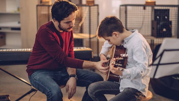 Boy teaching to play guitar in music school