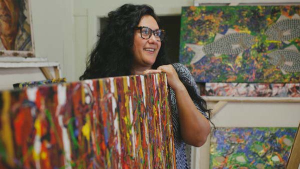 An Aboriginal woman smiles at the artist in his studio